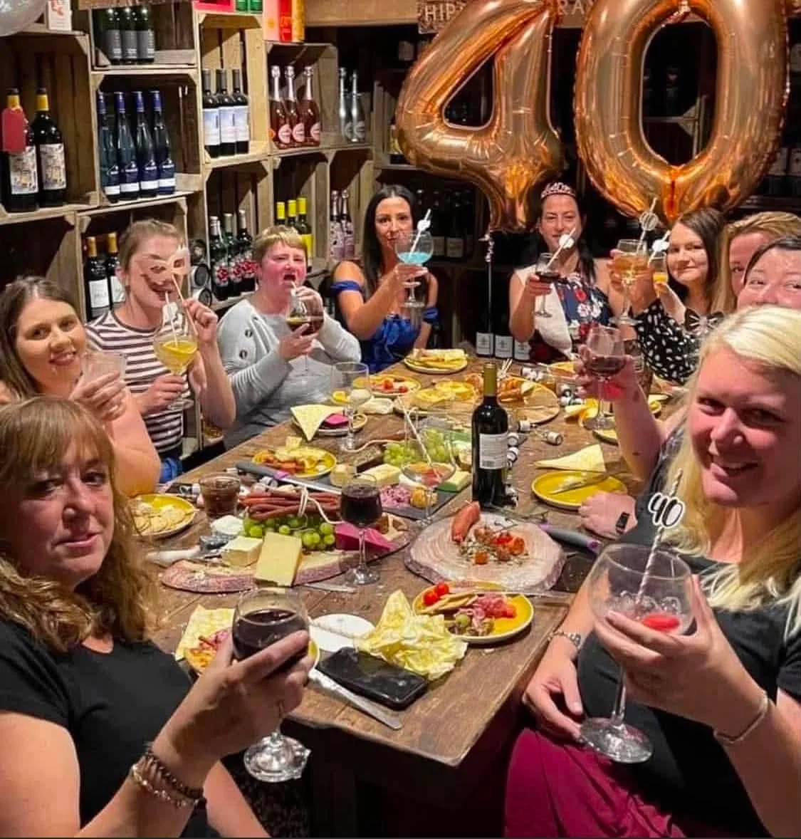 Friends raising their glasses around a birthday table with gold 40 balloons