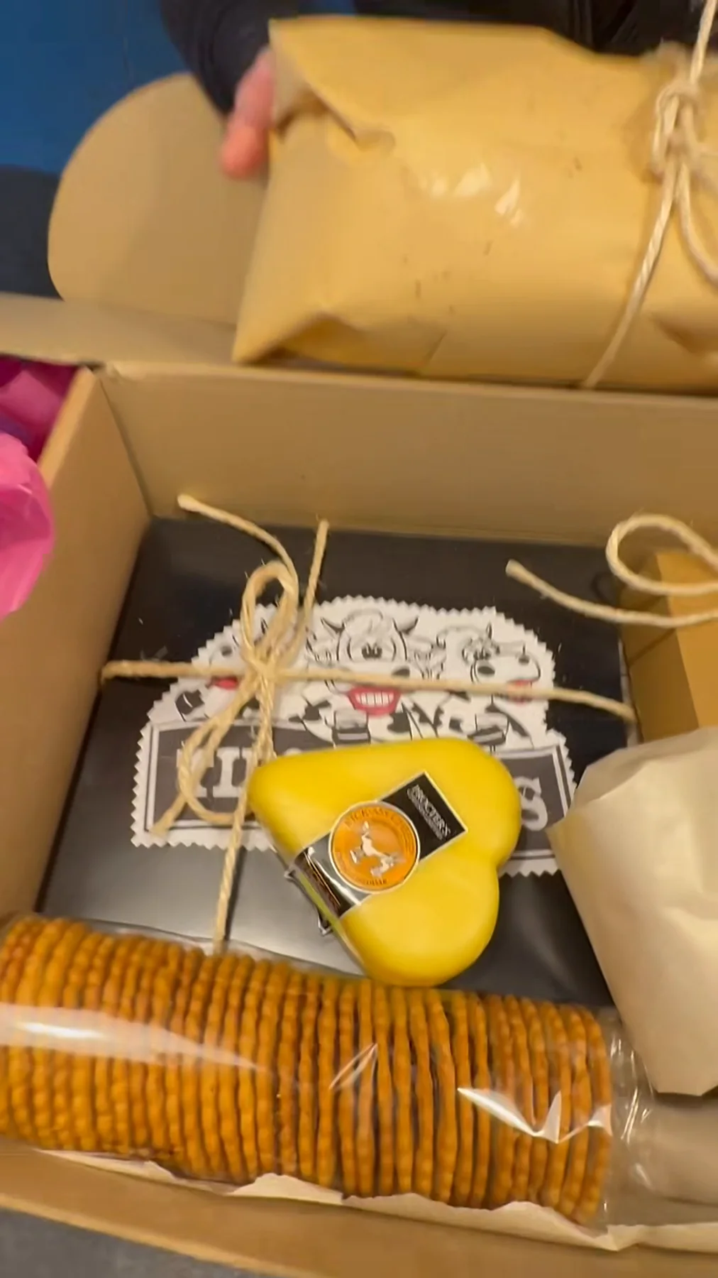 An open hamper box with a heart-shaped cheese, crackers and wrapped cheeses