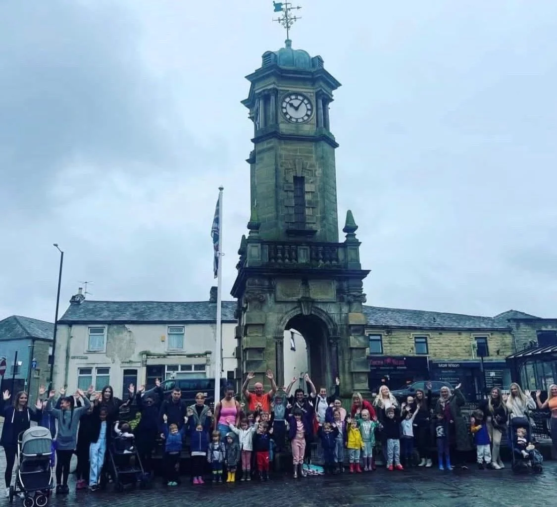 Families waving by the Great Harwood clock tower before a Nothing Is Impossible trip